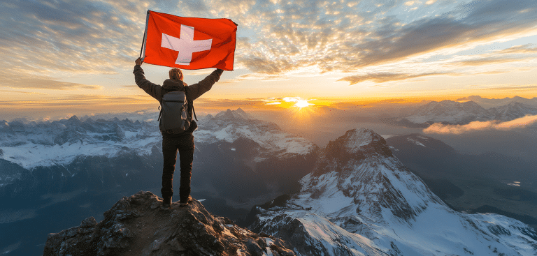 Von: kardaska/AdobeStock Person mit Schweizer Flagge auf einem Gipfel