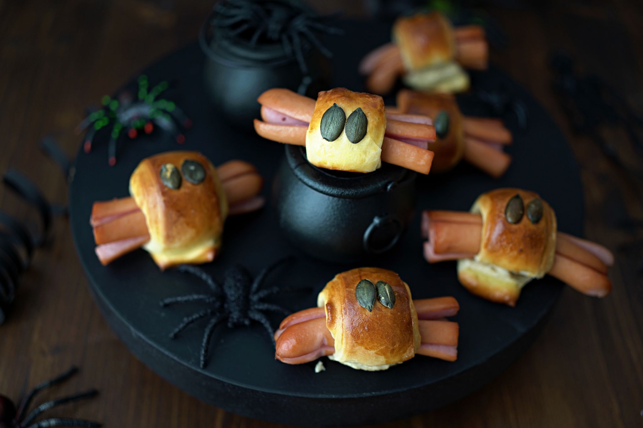 Für die Würstchenspinnen werden die an den Enden eingeschnittenen Wienerstückchen mit Teigstreifen umwickelt. Darauf drückt man je zwei Kürbiskerne als Augen und schiebt das Ganze in den Backofen.