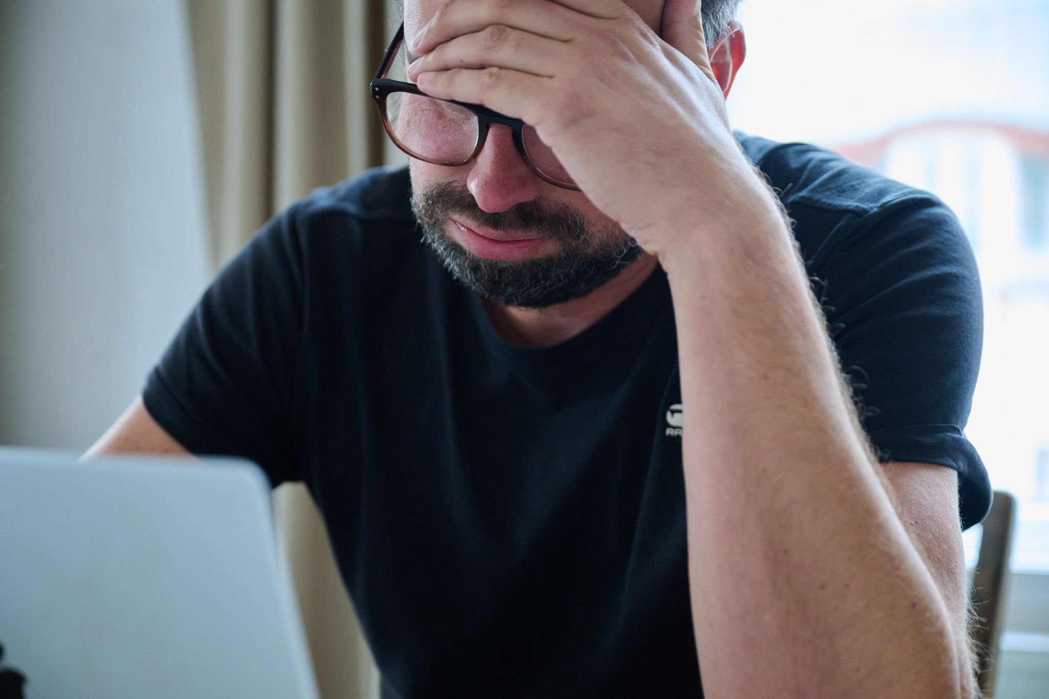 Ein Mann sitzt vor einem Laptop und seufzt.